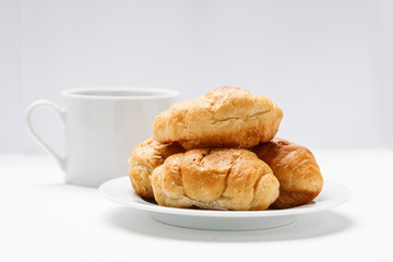 Fresh croissant in a white plate and coffee mug on a white table
