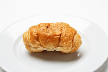 Single fresh croissant in a white plate on a white table