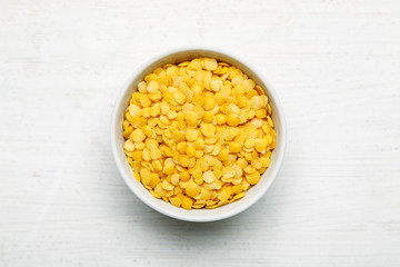 Yellow lentils in a white bowl on a white background, top view