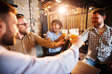 Joyful multicultural male friends clinking with draft beer in the local pub.