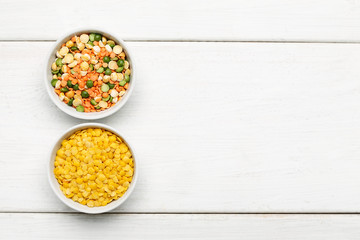 Different beans in bowls on a white wooden table, top view