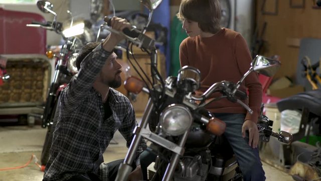 Father mentoring teenage son sitting on motorbike in garage. 