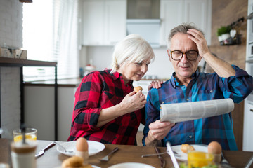 Fototapeta na wymiar Senior man reading newspaper during breakfast with wife