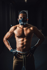 Fototapeta na wymiar african american athletic man in mask looking at camera and holds hands on belt. black man posing in gym. black background