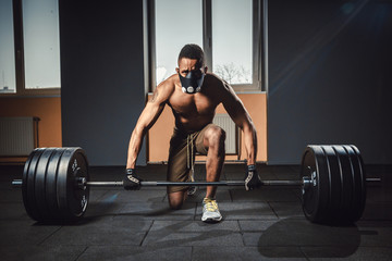 Fototapeta premium african american athletic man waiting and preparing before lifting heavy barbell looking at camera. fitness, sport, training, gym concept. deadlift with barbell in mask. bent over the barbell
