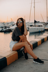 Fashion Portrait of Beautiful Sexy Girl. Posing on Yacht Club at Europe. Young Pretty Hipster Woman with Long Dark Brown Hair Color, Big Lips and Sunglasses. Film Color, Grain and Effects 