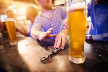 Crédence de cuisine en verre imprimé Bar Homme ivre prenant la clé de la voiture de la table du pub avec une bière pression devant. Vue rapprochée de la clé et des mains.