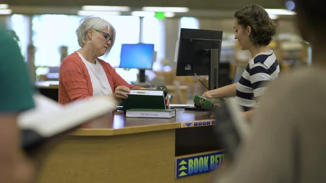 Students returning books to librarian in college library.