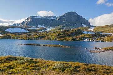 Magnificent view of a mountain plateau Hardangervidda with numerous lakes and rivers in summer time on snow mounts background, Norway national park