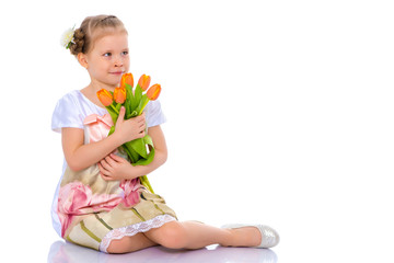 Little girl with bouquet of flowers sits on the floor.