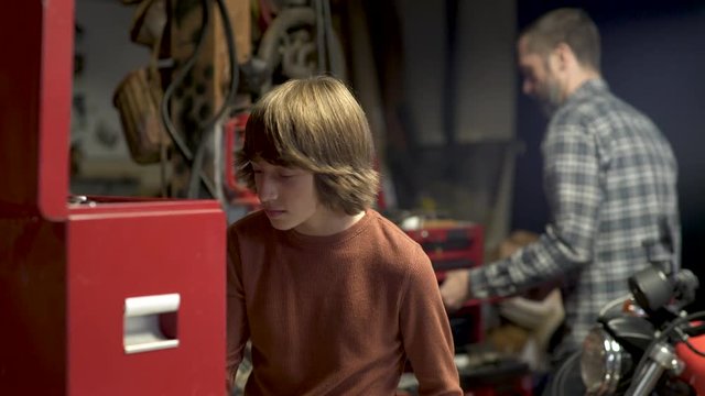 Son handing father wrench from toolbox in garage. 