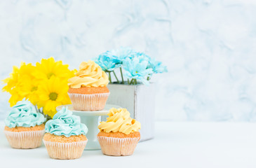 Cupcakes with yellow and blue cream decoration and bouquet of yellow chrysanthemum on pastel background.