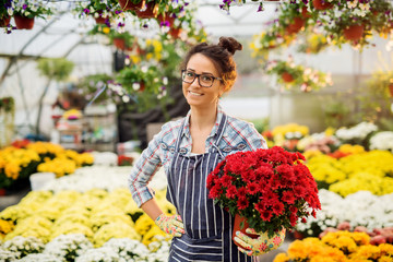 Beautiful pretty florist woman posing with red flowers in the colourful bright greenhouse.