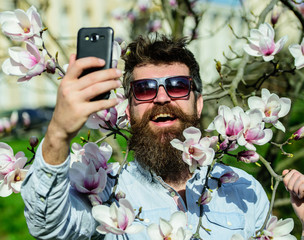 Hipster happy in stylish sunglasses, taking selfie photo, streaming video on smartphone. Blogger...