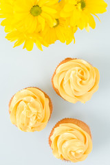 Cupcakes with yellow cream decoration and bouquet of fresh chrysanthemums on blue pastel background.