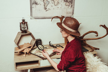 retro style woman in hat with magnifying glass sitting at table with map