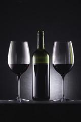 glasses filled with red wine and wine bottle in middle on black