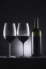 glasses filled with red wine and wine bottle on black