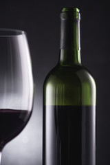 close-up shot of blurred glass filled with red wine on foreground and wine bottle on black
