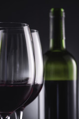 close-up shot of glasses filled with red wine and wine bottle blurred on background