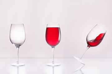 empty wineglass with full and inclined in row on reflective surface and on white