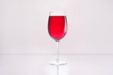 glass full of red wine on reflective surface and on white