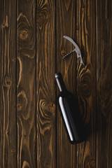 top view of bottle of red wine and corkscrew on wooden table