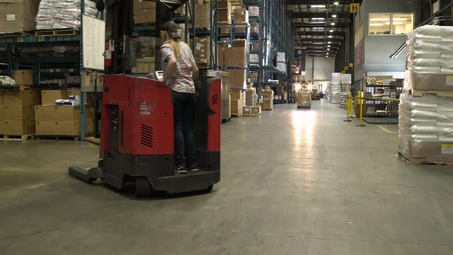 Team driving and operating machinery by warehouse aisle.