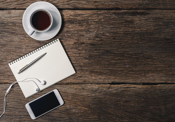 Office wooden desk with pen, notepad, coffee cup, smartphone and earphones. Top view