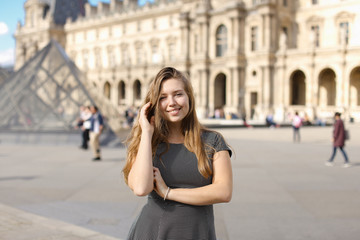 Young woman standing near Louvre Pyramid and smiling. Concept of traveling to Europe.