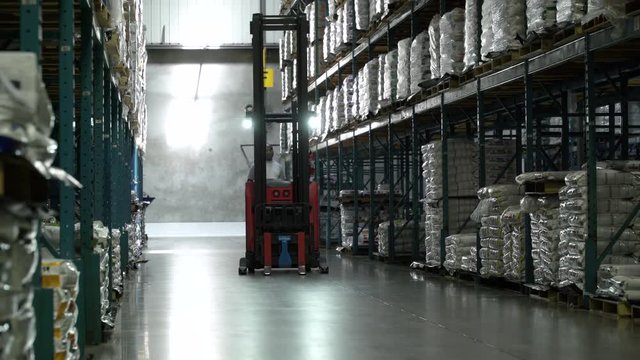 Man driving forklift machinery in aisle of warehouse.