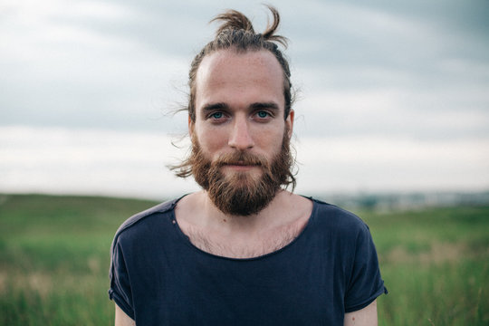 Portrait of a handsome man with a top knot and beard standing in a meadow