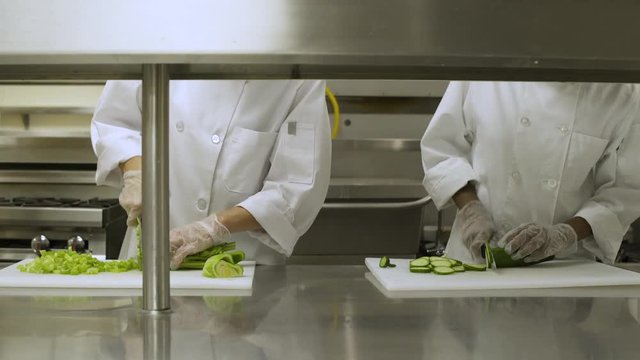 Students chopping fresh salad vegetables in commercial kitchen.