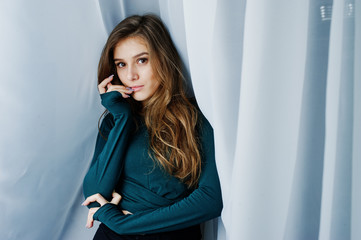 Handsome brunette girl wear on green, posing at curtains. Studio model portrait.