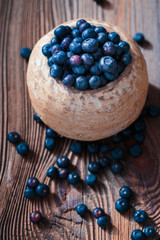 Freshly gathered blueberries put into old ceramic bowl. Some fruits freely scattered on old wooden table