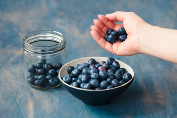 Woman putting freshly gathered blueberries from a jar into a small bowl