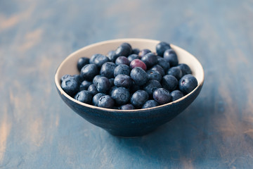Small bowl full of fresh blueberries put on painted in blue table