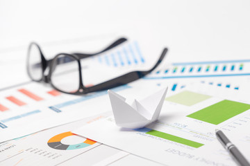 Obraz premium Boats made of paper graph on notebook with glasses and pen.Business Analysis concept.