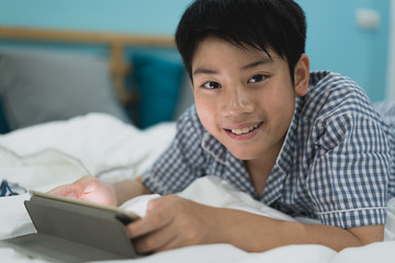 Cut boy lying on the bed with a table. Child playing with digital tablet lying on a bed.