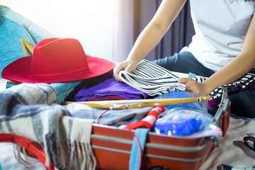 Travel and vacation concept, happiness woman packing stuff and a lot of clothes into suitcase on bed prepare for her travel and journey trip