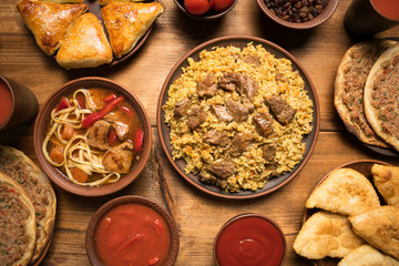 Delicious Asian pilaf and beef soup lagman on a brown plate in rustic style. Uzbek restaurant concept. Assorted Uzbek food set, pilaf, rice, soup with beef, lagman, turkish pizza, dried meat, samsa.