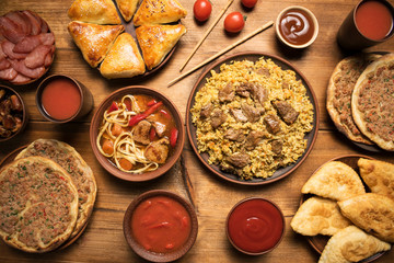 Bowls and plates with middle eastern or arabic dishes on rustic wooden background. Pilaf, rice, soup with beef, lagman, turkish pizza, samsa, pasties, dates, raisins, tomatoes, dried meat. Flat lay.