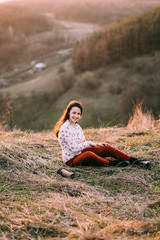 Girl lies in the mountains at sunset with gold hair. She resting wearing stylish fall outfit. Concept travel and relax