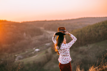 Portrait of a attractive young girl with a hat in the mountains at sunset. She resting and sitting wearing stylish fall outfit. Concept travel