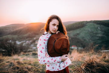 Portrait of a attractive young girl with a hat in the mountains at sunset. She resting and sitting wearing stylish fall outfit. Concept travel