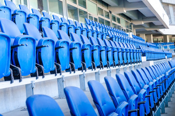 Sitting fans colored plastic chairs at the football stadium background. Empty stadium football field green grass for soccer athletics arena.