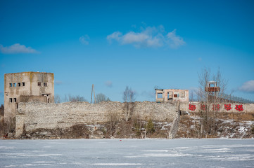 Fototapeta na wymiar View of abandoned prison located in small lake with blue clear water in Rummu, Estonia. Ruins on ex industry place in old stone building. Wall with a lookout post. Winter.