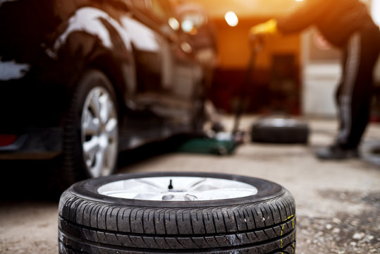New tire laying on the pavement near the mechanic ready to replace the one on a car.