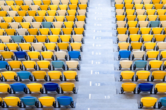 Sitting fans colored plastic chairs at the football stadium background. Empty stadium football field green grass for soccer athletics arena.