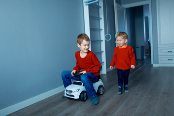 Two happy children riding on baby car in room, indoors.